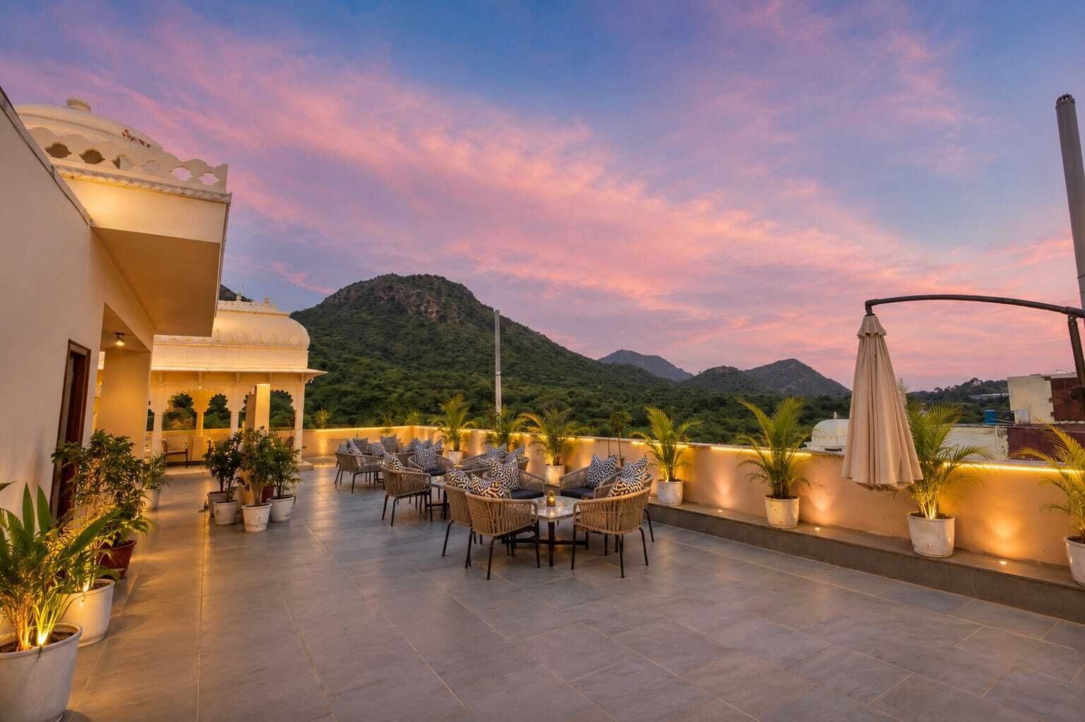 A rooftop terrace with outdoor seating, potted plants, and a view of mountains.