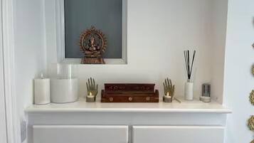 Una consola blanca con un icono religioso enmarco, velas, una pequeña estatua y una caja decorativa.