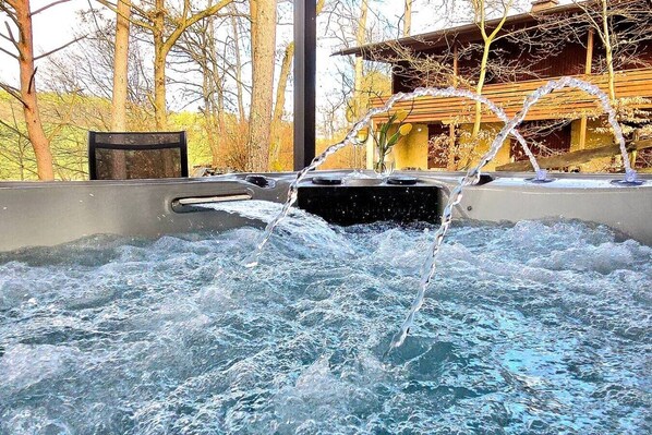 A hot tub with water flowing into it, surrounded by trees and a wooden building.