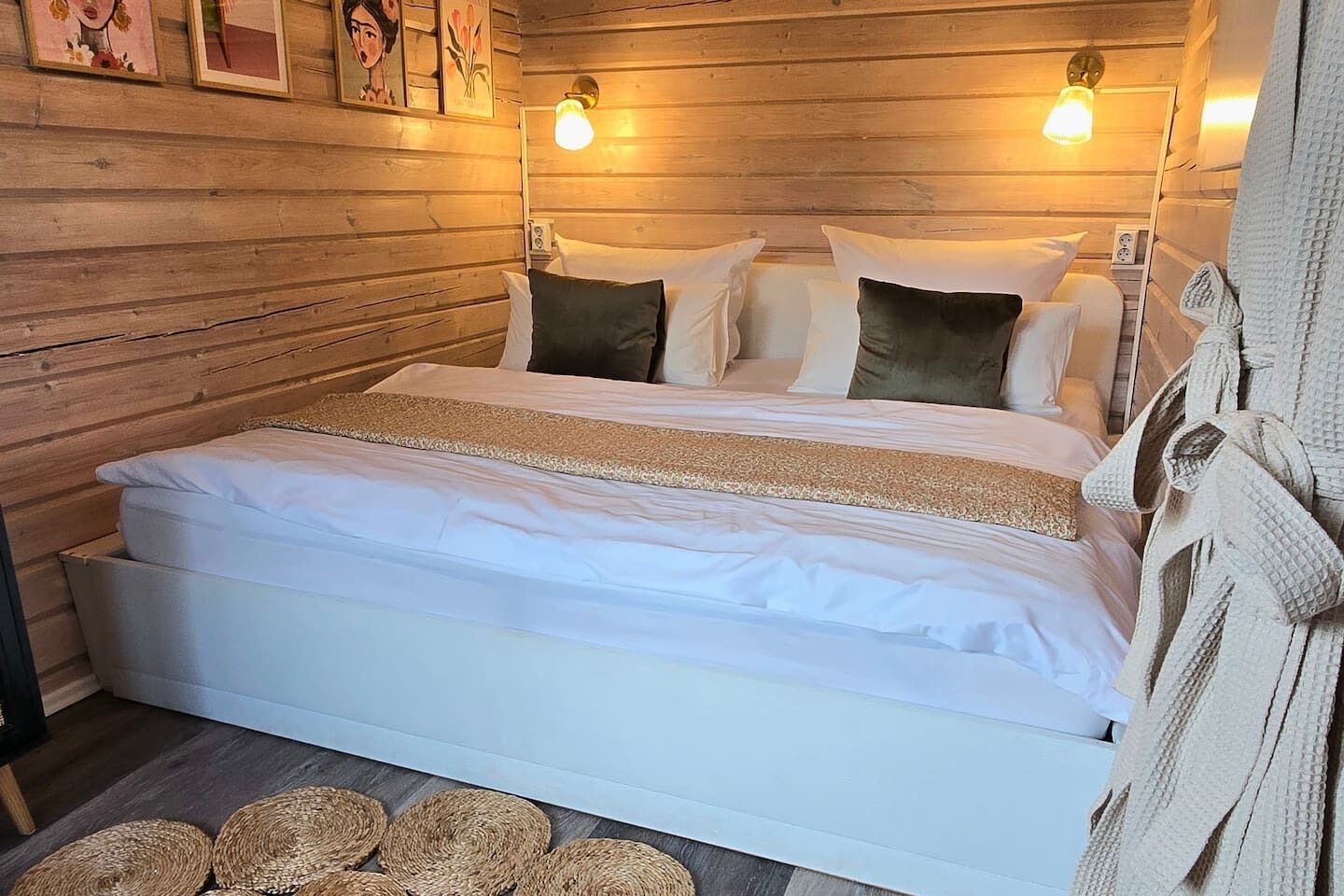 A wooden-paneled room with a bed, two wall-mounted lights, and a woven rug.