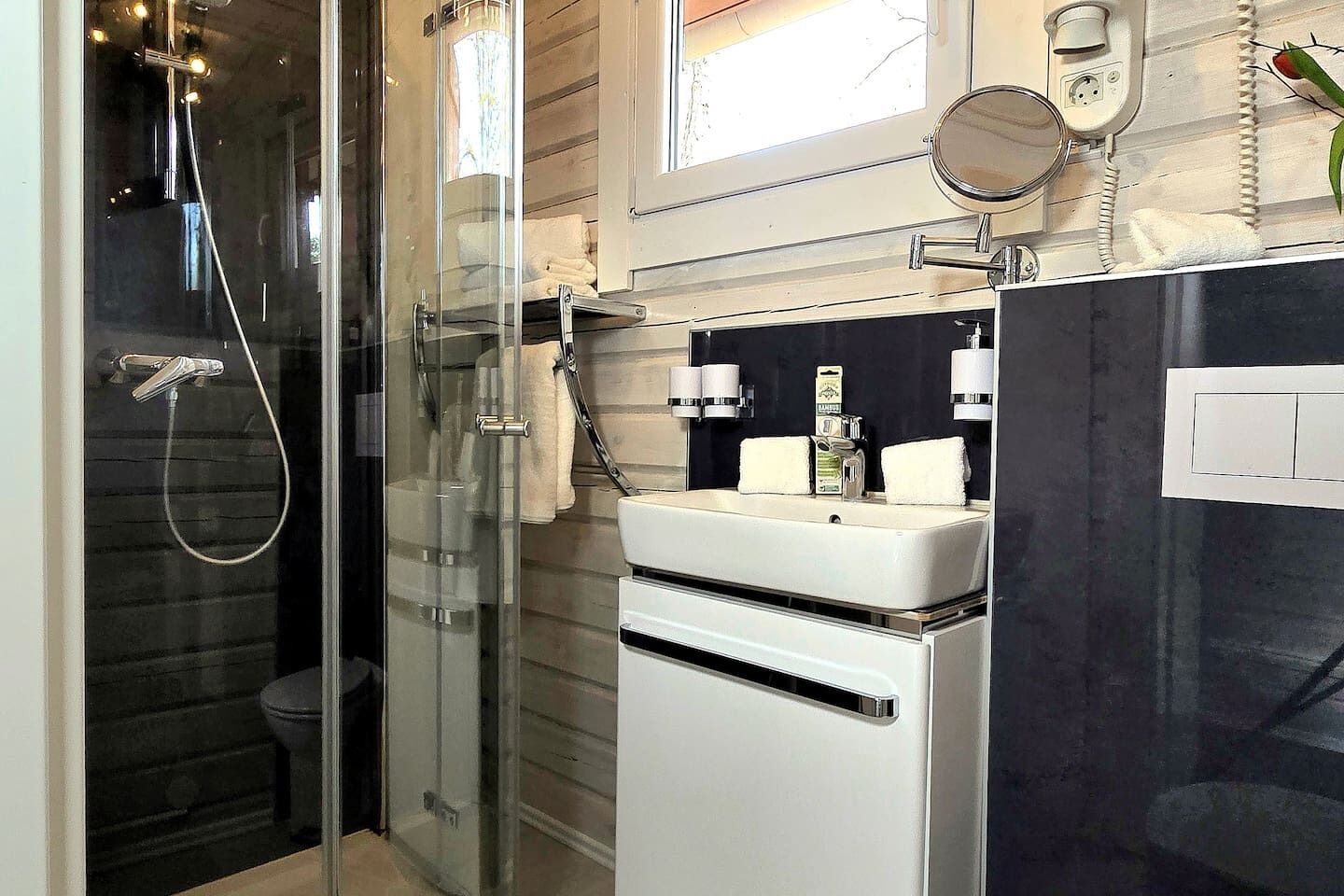 Ein modernes Badezimmer mit Duschkabine aus Glas, einem weißen Waschbecken mit Spiegel und einer Toilette.