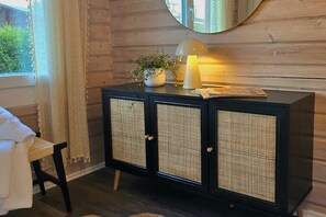 Et sort træskab med flettede døre, et lille bord med en lampe og et vindue med gardiner.