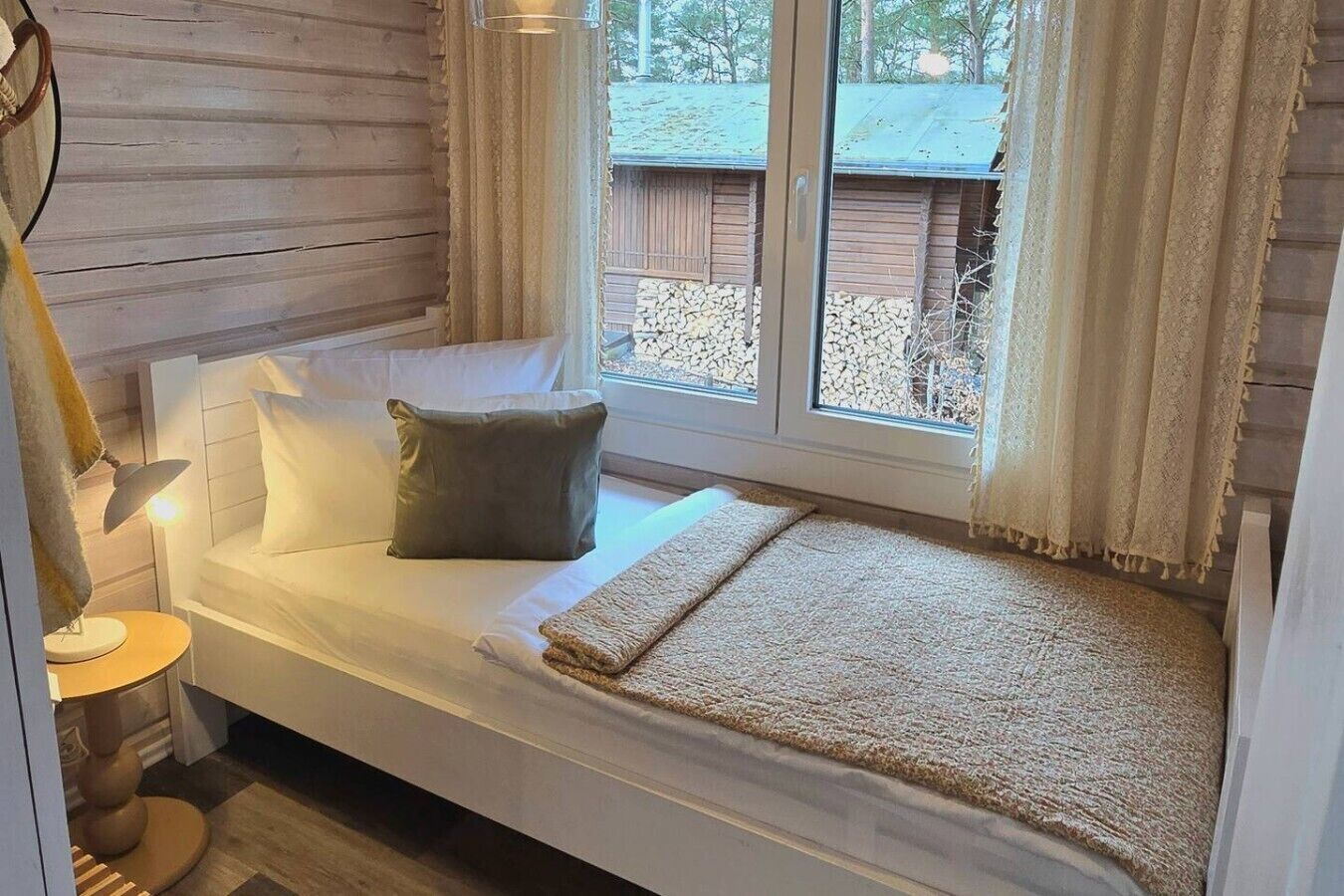 Ein kleines, gemütliches Zimmer mit einem Einzelbett, einem Fenster mit Vorhängen und einer Lampe auf einem Nachttisch.