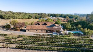 A vineyard with rows of grapevines, a stone building with a tiled roof, and a swimming pool. - Guesthouse “Chez Fayol” with Shared Pool, Communal Garden, and Wi-Fi (Montagnac-la-Crempse)