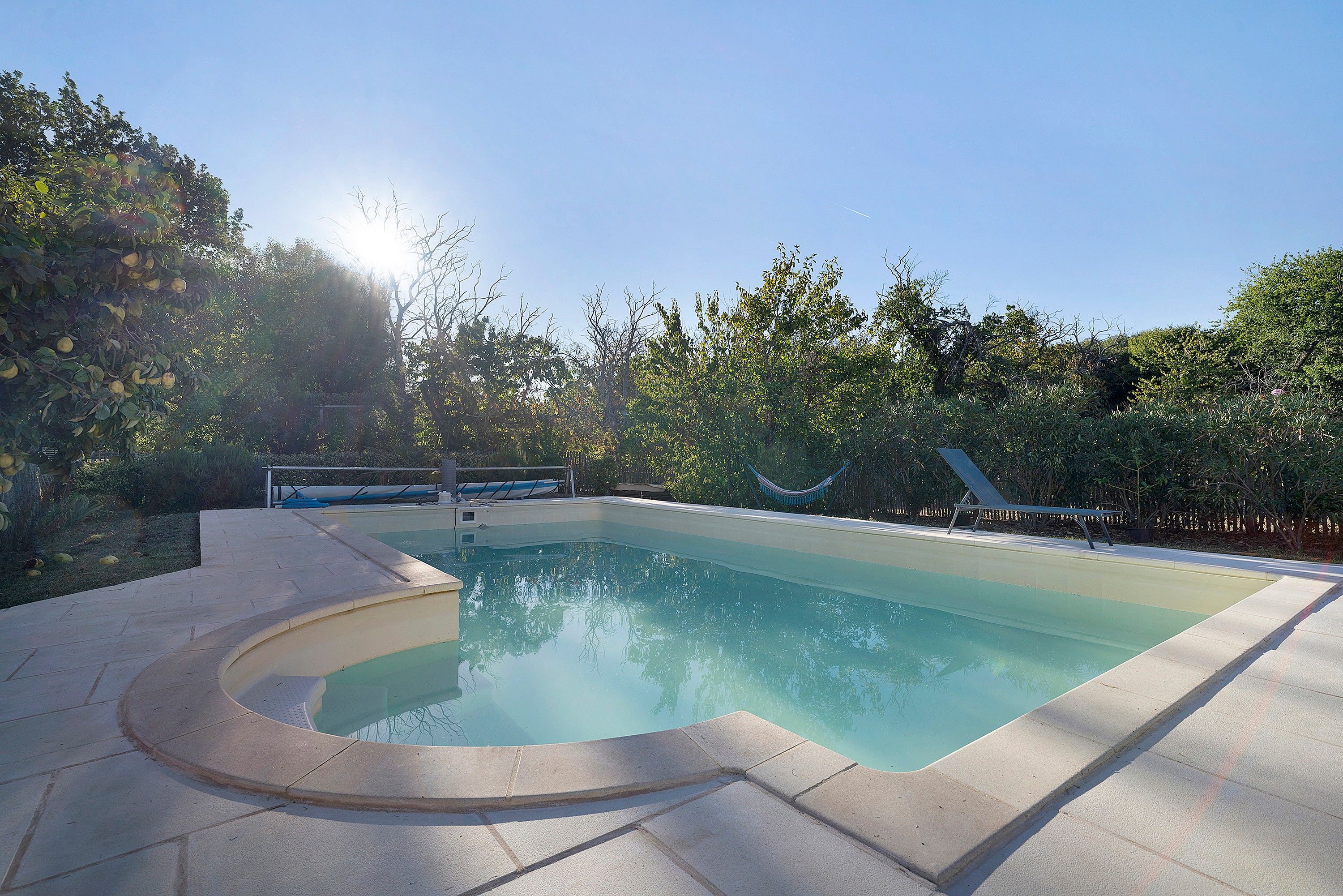 Una piscina de borde curvo, rodeada por un solárium empedrado y exuberante vegetación.