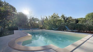 Una piscina de borde curvo, rodeada por un solárium empedrado y exuberante vegetación.