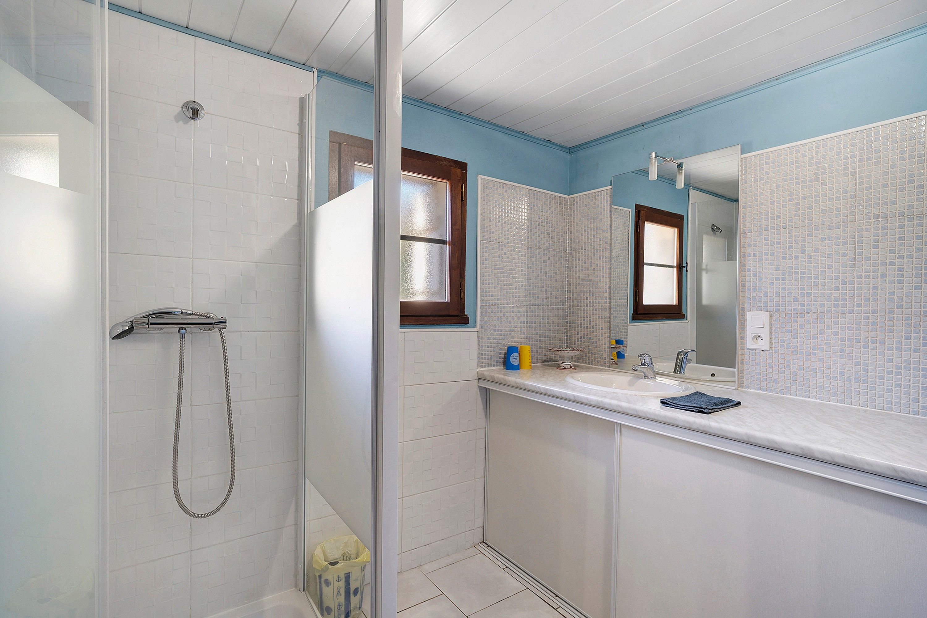 Ein Badezimmer mit Dusche, Waschbecken, Spiegel und Fenster.