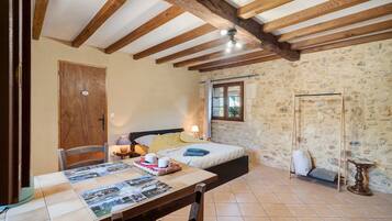 A room with a bed, a table with a placemat, a wooden door, and a stone wall.