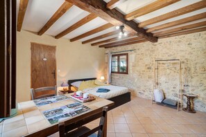 Ein Zimmer mit einem Bett, einem Tisch mit Unterlage, einer Holztür und einer Steinwand.