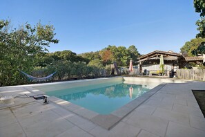A swimming pool with a tiled deck, surrounded by trees and a hammock.