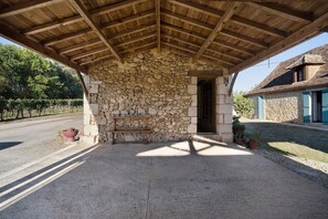 A covered outdoor seating area with a stone wall, a bench, and a door leading to a building. - Guesthouse “Chez Fayol” with Shared Pool, Communal Garden, and Wi-Fi (Montagnac-la-Crempse)