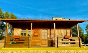 Une cabane en bois dotée d’un porche, d’une porte et d’une petite dépendance attenante.