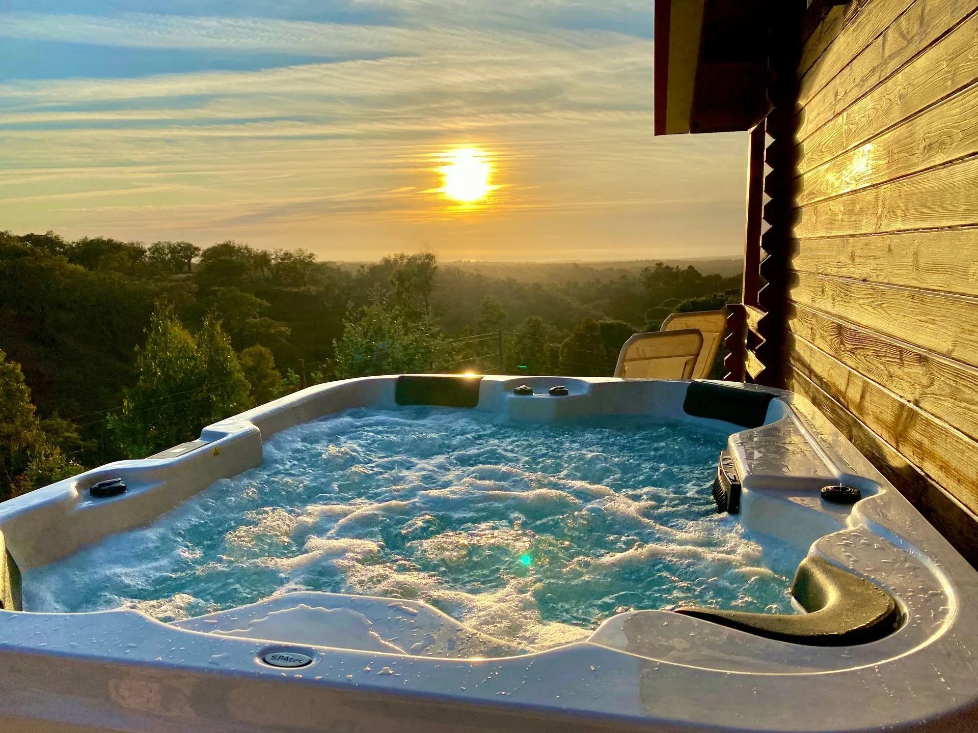 Uma banheira de hidromassagem com vista para o pôr do sol e árvores ao redor.