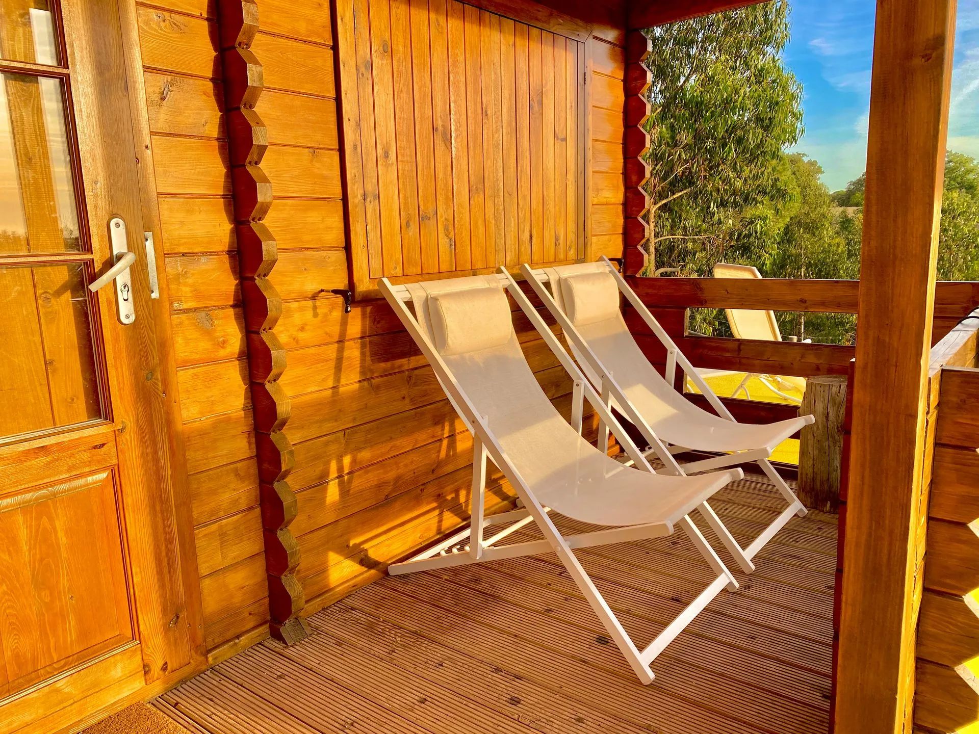 Une terrasse en bois avec deux chaises longues blanches et une porte en bois.
