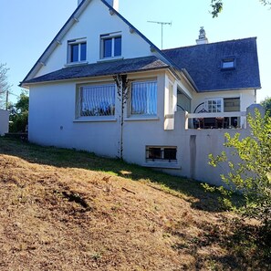 A two-story house with a sloped roof, a small porch, and a visible chimney. - Charming house 900 meters from the ocean (Plouha)