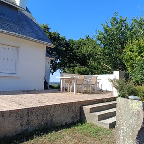 Ein weißes Gebäude mit einem Ziegeldach, einer gepflasterten Terrasse und einem Tisch mit Stühlen.