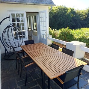 Een terras met een houten tafel en stoelen, een hangstoel en uitzicht op de tuin.
