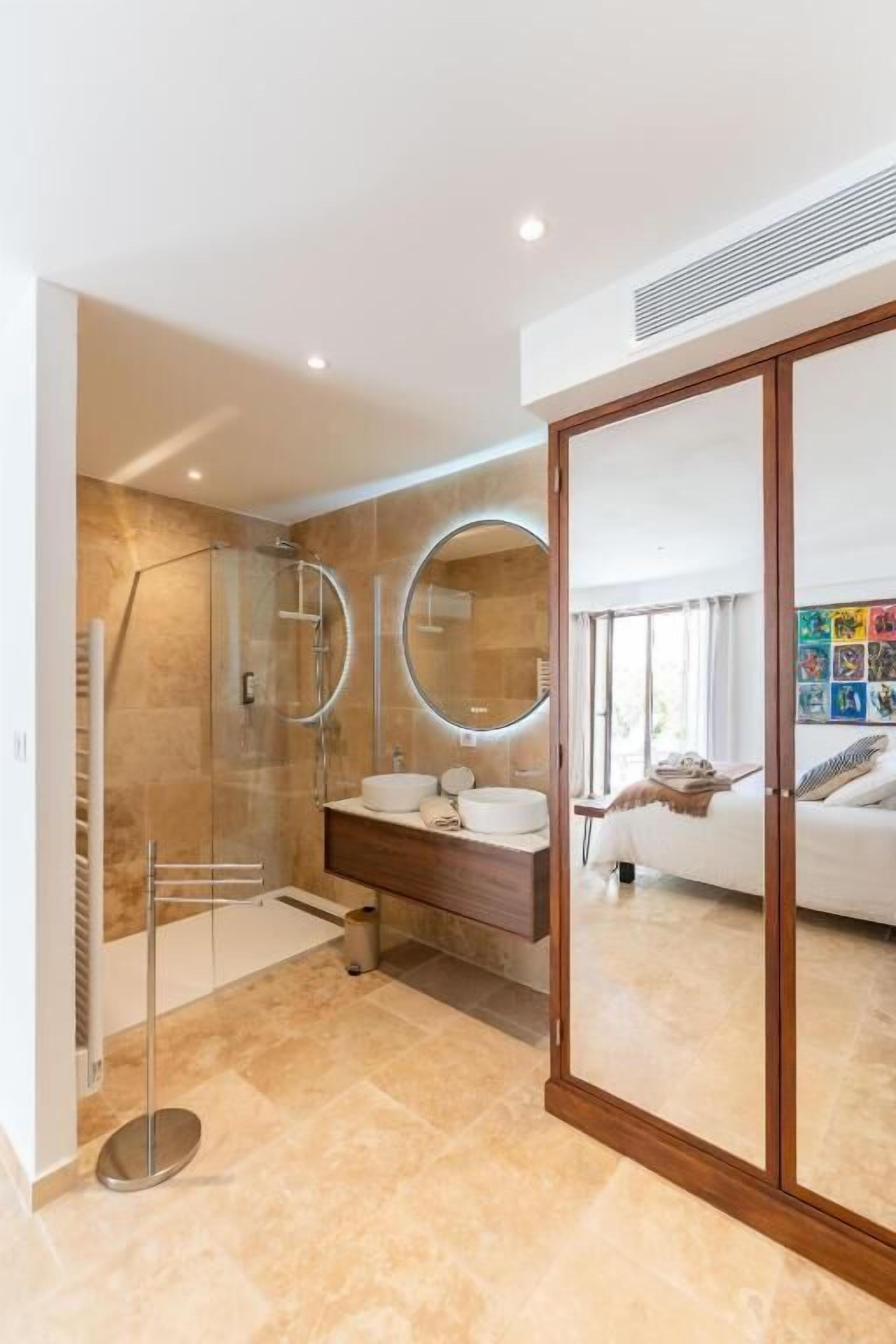 Un baño moderno con ducha envuelta en vidrio, tocador con espejo y un espejo grande.