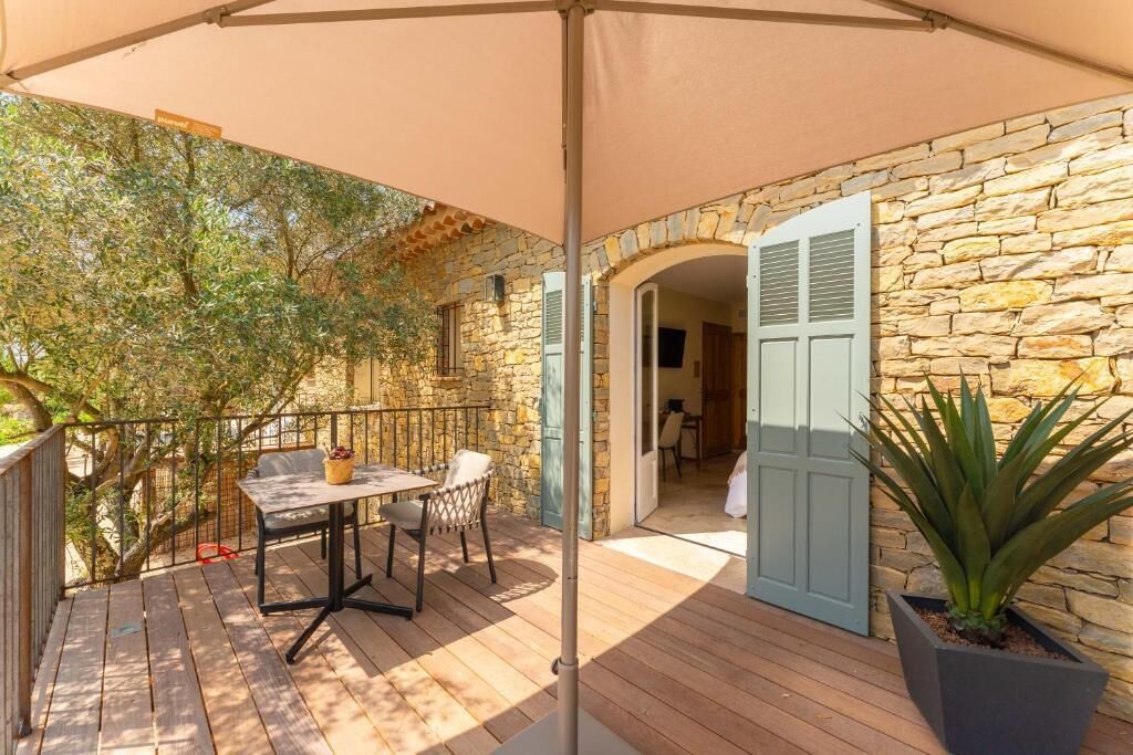 A wooden deck with a table and chairs, a stone wall, and a door with shutters.