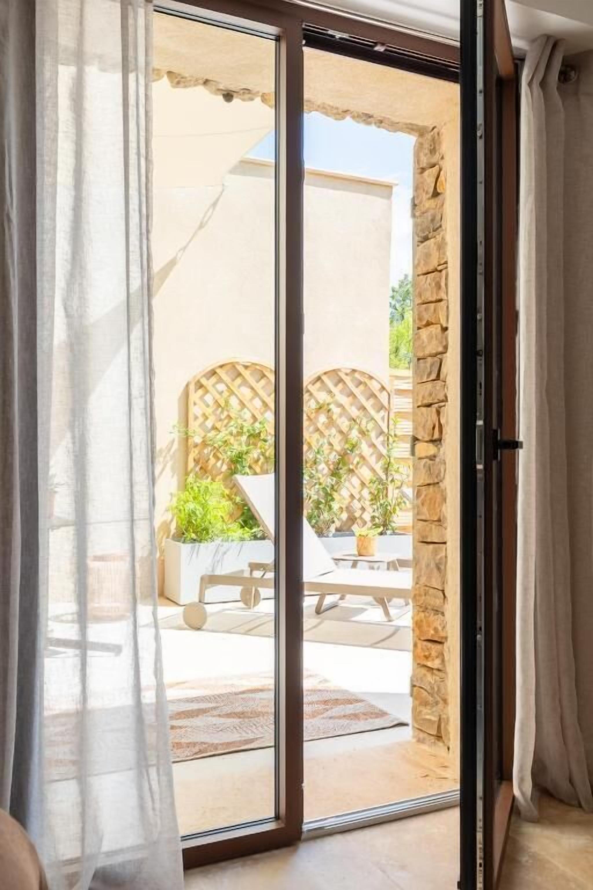 Puerta corrediza de vidrio que da a un patio exterior con pared de piedra, mesa de madera y una silla con cojín.