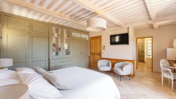 Ein Schlafzimmer mit einem großen Bett, einem Kleiderschrank, zwei Stühlen, einem Fernseher und einem durch eine offene Tür einsehbaren Badezimmer.