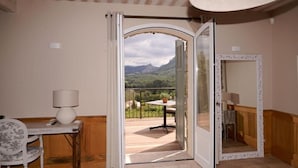 A room with a view of mountains through an open door, a table with a lamp, and a mirror. - MAISON BAOU ET CHOCOLAT (La Cadiere-d'Azur)