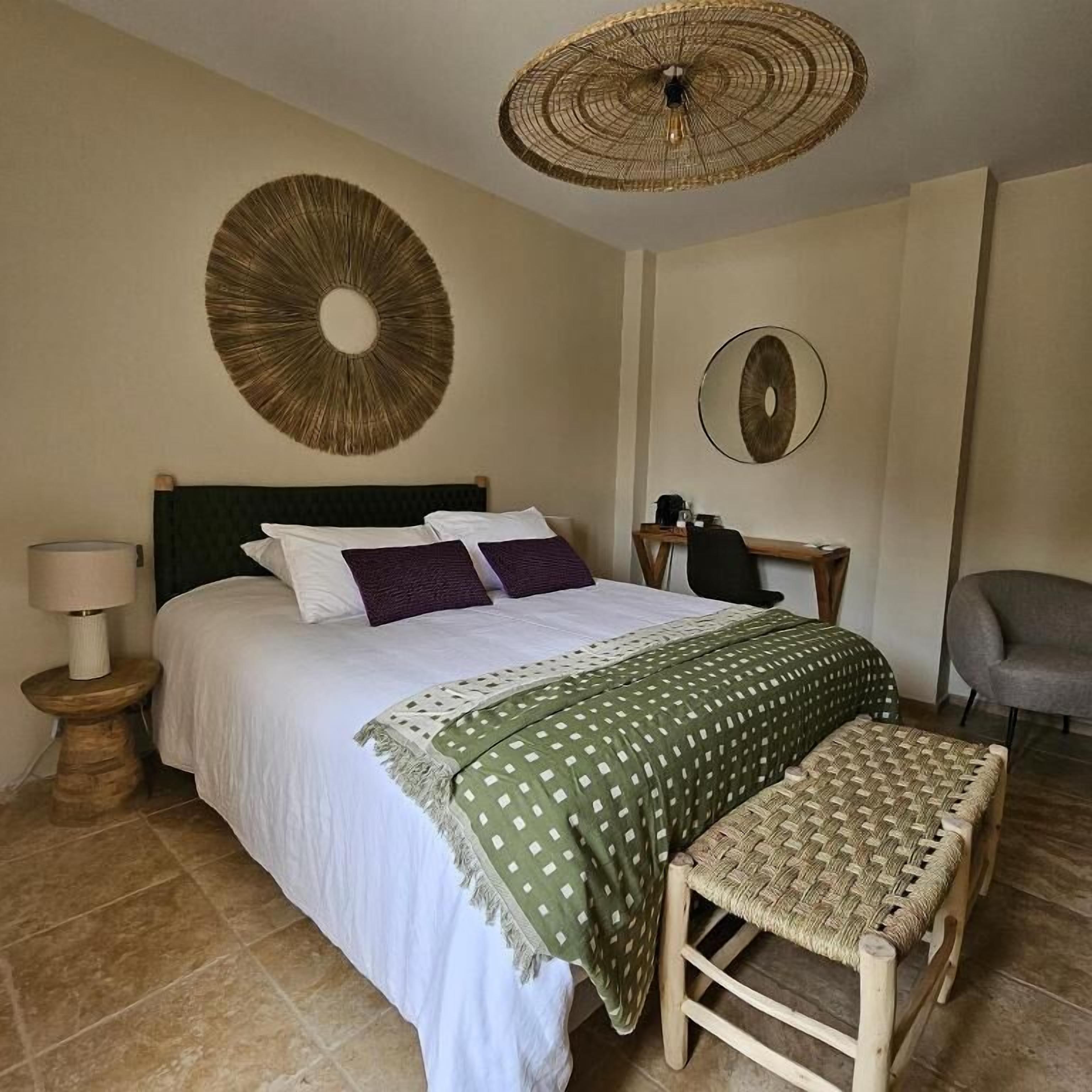 A bedroom with a bed, a bedside table, a chair, and a woven bench.