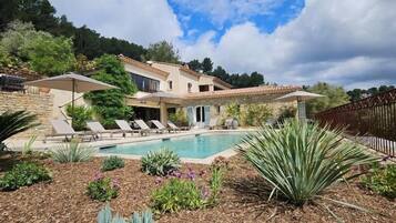 Eine Villa mit Schwimmbad, umgeben von einem angelegten Garten und einem Holzzaun.