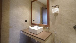 A bathroom with a marble wall, a wooden-framed mirror, a white sink, and a towel rack.