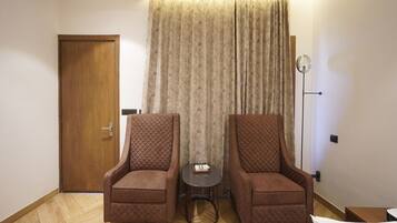 A hotel room with two armchairs, a small table, a floor lamp, and a bed.
