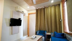 A room with a flat-screen TV mounted on the wall, a wooden table, a blue sofa, and a curtain covering a window.
