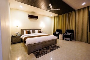 Quarto de hotel moderno com uma cama grande, duas poltronas, um ventilador de teto e uma televisão de tela plana.