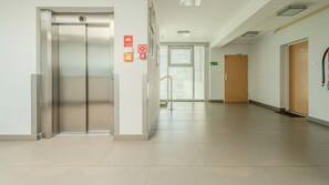 A clean, modern hallway with an elevator, a fire alarm, and a door with a green exit sign. - Apartamenty Sun & Snow SeaSide  (Świnoujście)