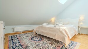 Une chambre à coucher avec un lit, un radiateur, un tapis à motifs et une lucarne.