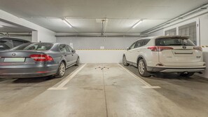 Eine Parkgarage mit zwei Autos in gegenüberliegenden Fahrbahnen, gekennzeichneten Parkfeldern und einem Lüftungssystem an der Decke.