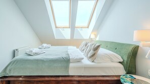 A bedroom with a sloped ceiling, a bed with a green headboard, white bedding, and two windows. - Apartamenty Sun & Snow SeaSide  (Świnoujście)