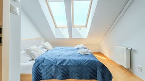 Ein Schlafzimmer mit Bett, Kissen, Heizkörper und Oberlichtern.