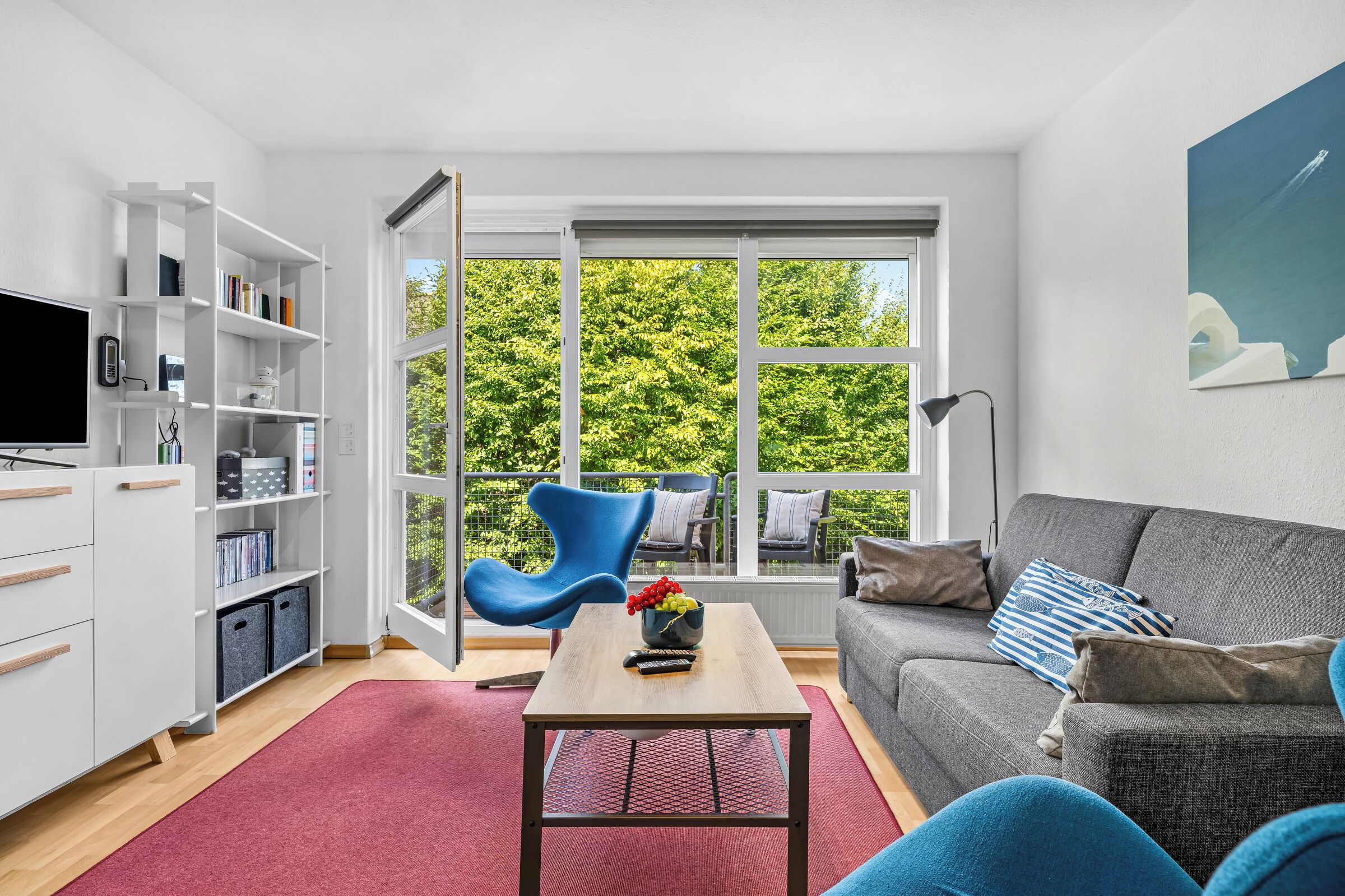 Un salon moderne avec un canapé gris, un fauteuil bleu, une table basse en bois et une bibliothèque.