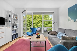 A modern living room with a grey sofa, a blue armchair, a wooden coffee table, and a bookshelf. - Buntfisch – A stunning maisonette flat just 300 metres from the Baltic Sea (Schönberg (Holstein))