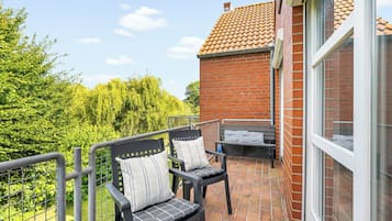 Ein Balkon mit zwei Stühlen und einem kleinen Tisch, mit Blick auf ein Backsteingebäude und Grünflächen.