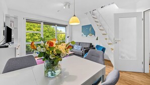A modern living space with a dining area, a staircase, and a view of greenery outside. - Buntfisch – A stunning maisonette flat just 300 metres from the Baltic Sea (Schönberg (Holstein))