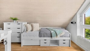 A bedroom with a sloped ceiling, a bed with storage drawers, a bedside table with a plant, and a window with a view. - Buntfisch – A stunning maisonette flat just 300 metres from the Baltic Sea (Schönberg (Holstein))