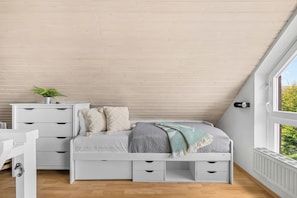 A bedroom with a sloped ceiling, a bed with storage drawers, a bedside table with a plant, and a window with a view. - Buntfisch – A stunning maisonette flat just 300 metres from the Baltic Sea (Schönberg (Holstein))
