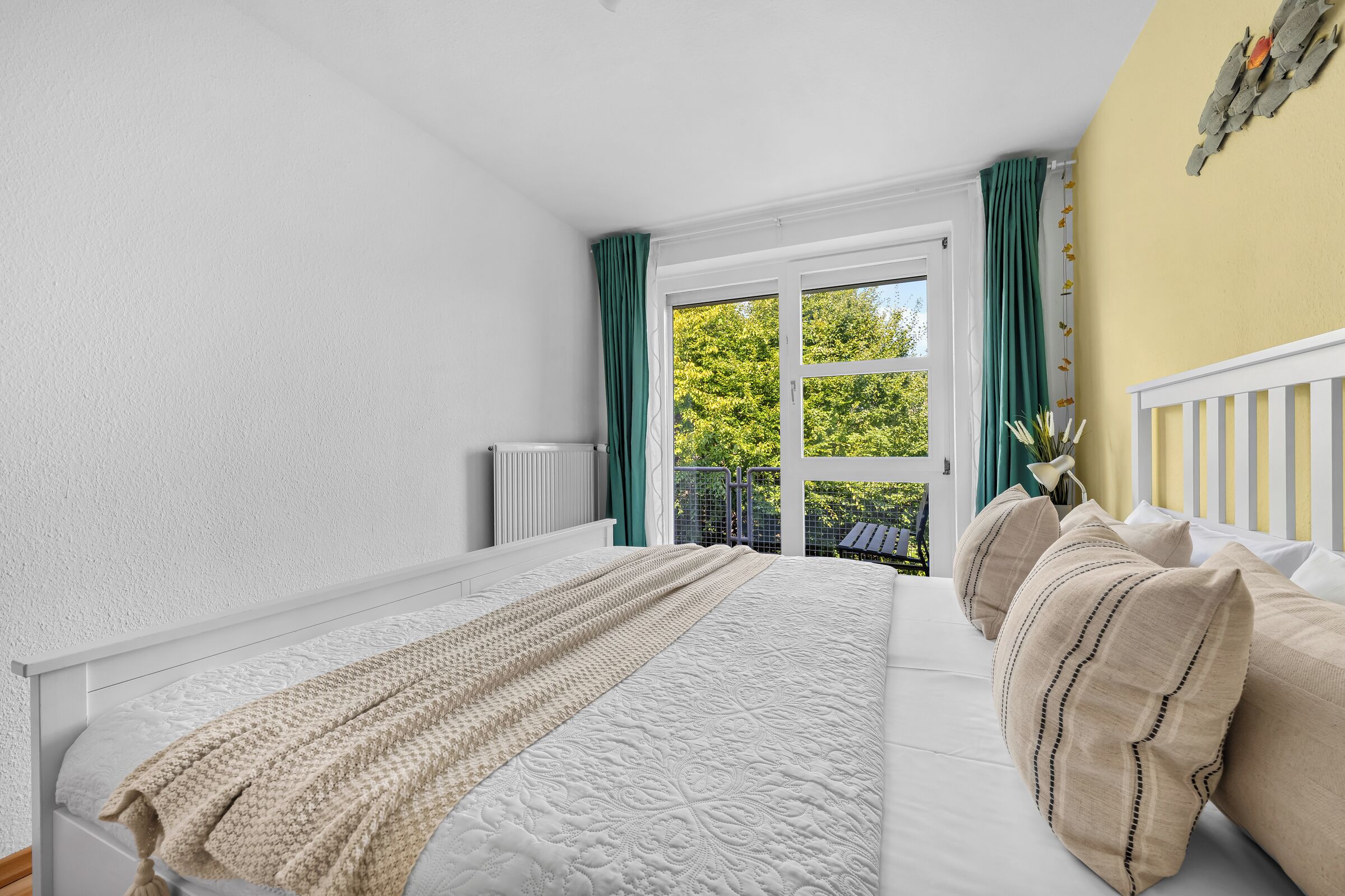 Una camera da letto con un letto, un termosifone, una finestra con tende e vista sul verde.