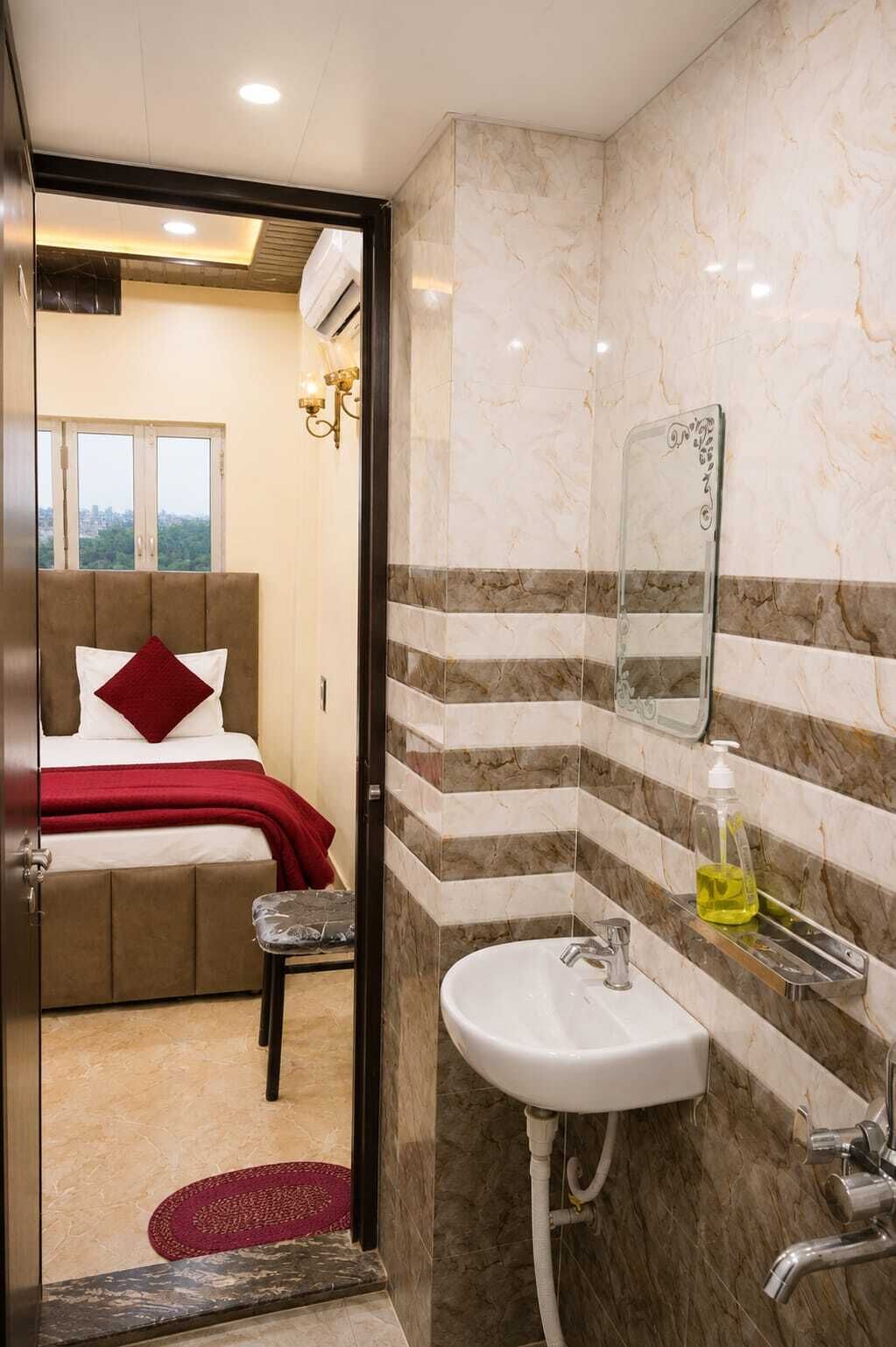 A hotel room with a bed, a bathroom with a sink and mirror, and a view of the city through a window.