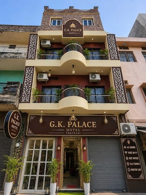 Un hotel con un cartel que dice 'G.K. Palace Hotel' y un letrero que anuncia comodidades como habitaciones con aire acondicionado, Wi-Fi gratuito, agua caliente, servicio 24 horas y un café en la azotea.
