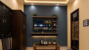 A modern interior with a flat-screen TV mounted on a wall, a wooden bench, and a dark blue accent wall. - Gk Palace (Varanasi)