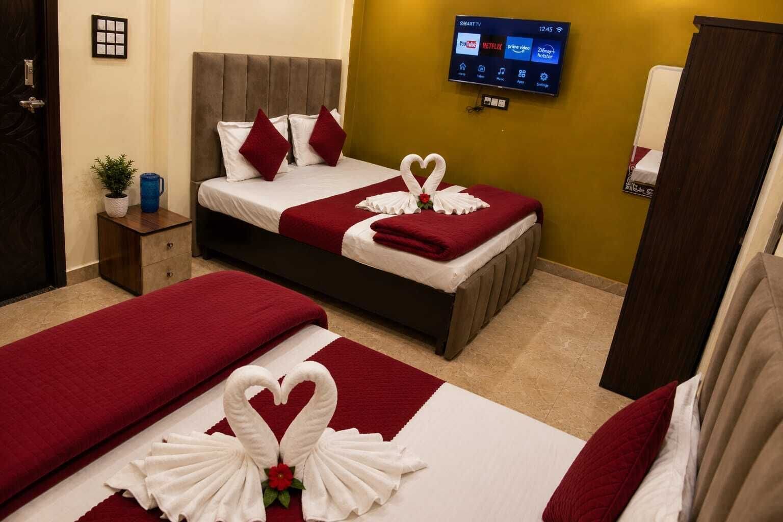 Habitación de hotel con dos camas, televisor montado en la pared y alfombra roja.