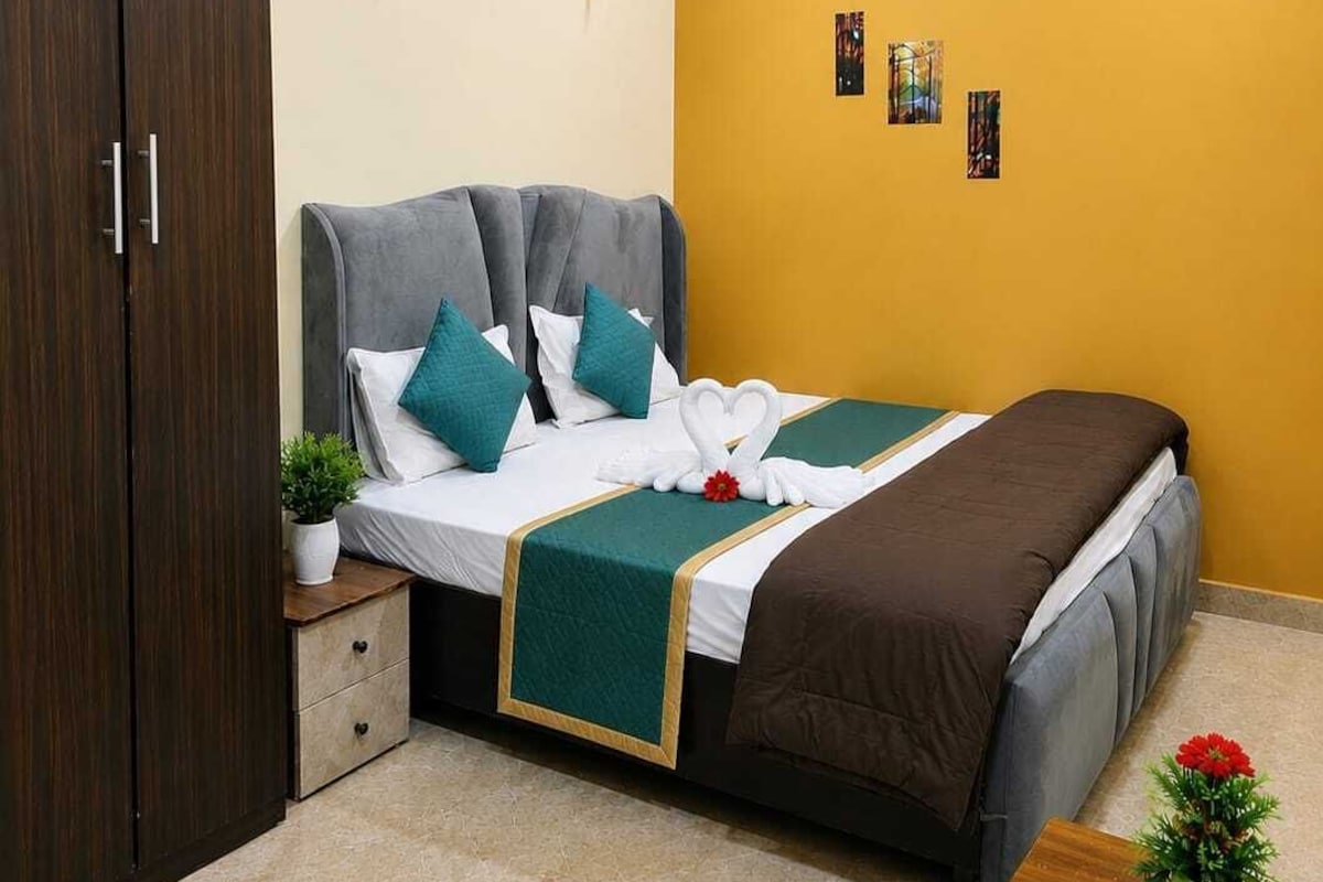 Una habitación de hotel con cama, armario, mesita de noche con planta y ventilador de techo.