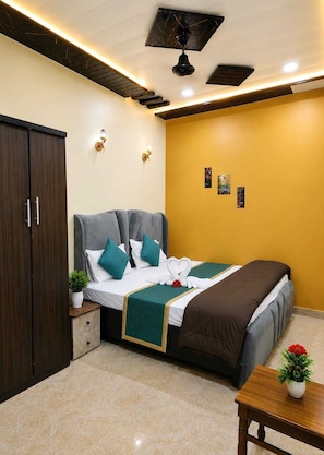 Una habitación de hotel con cama, armario, mesita de noche con planta y ventilador de techo.